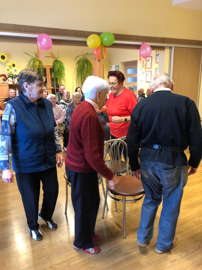 Grupa Seniorów chodzi wokół krzeseł, grają w grę kto pierwszy siądzie na stołku