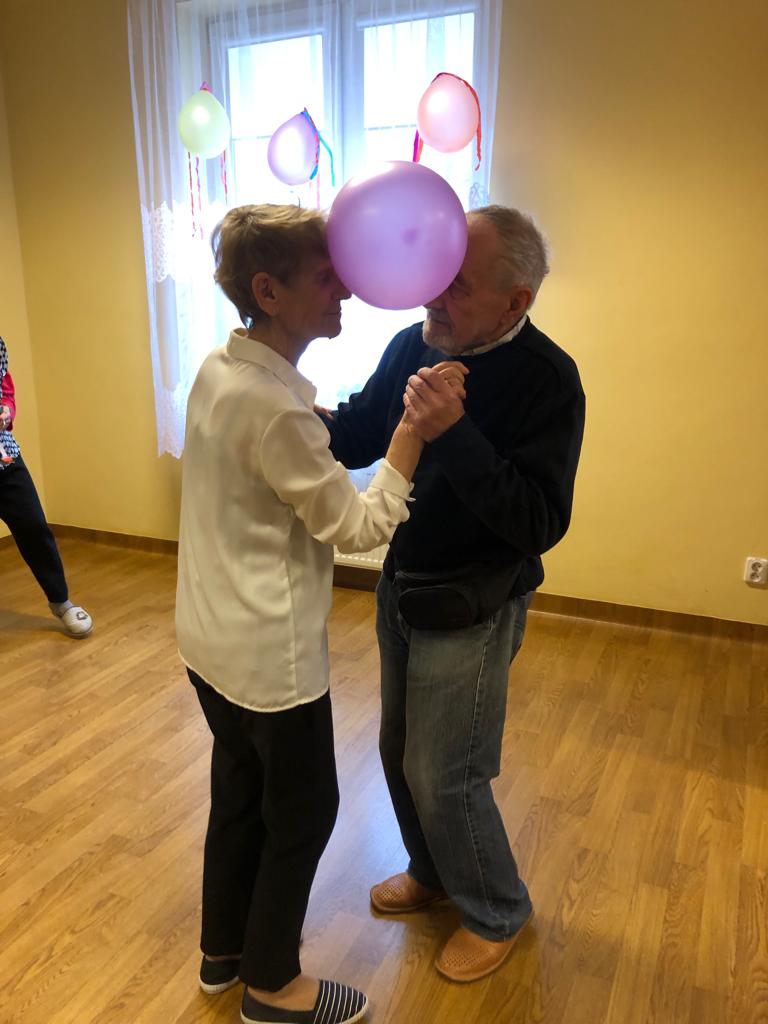 Para Seniorów tańczy, pomiędzy głowami starają się utrzymać balonik