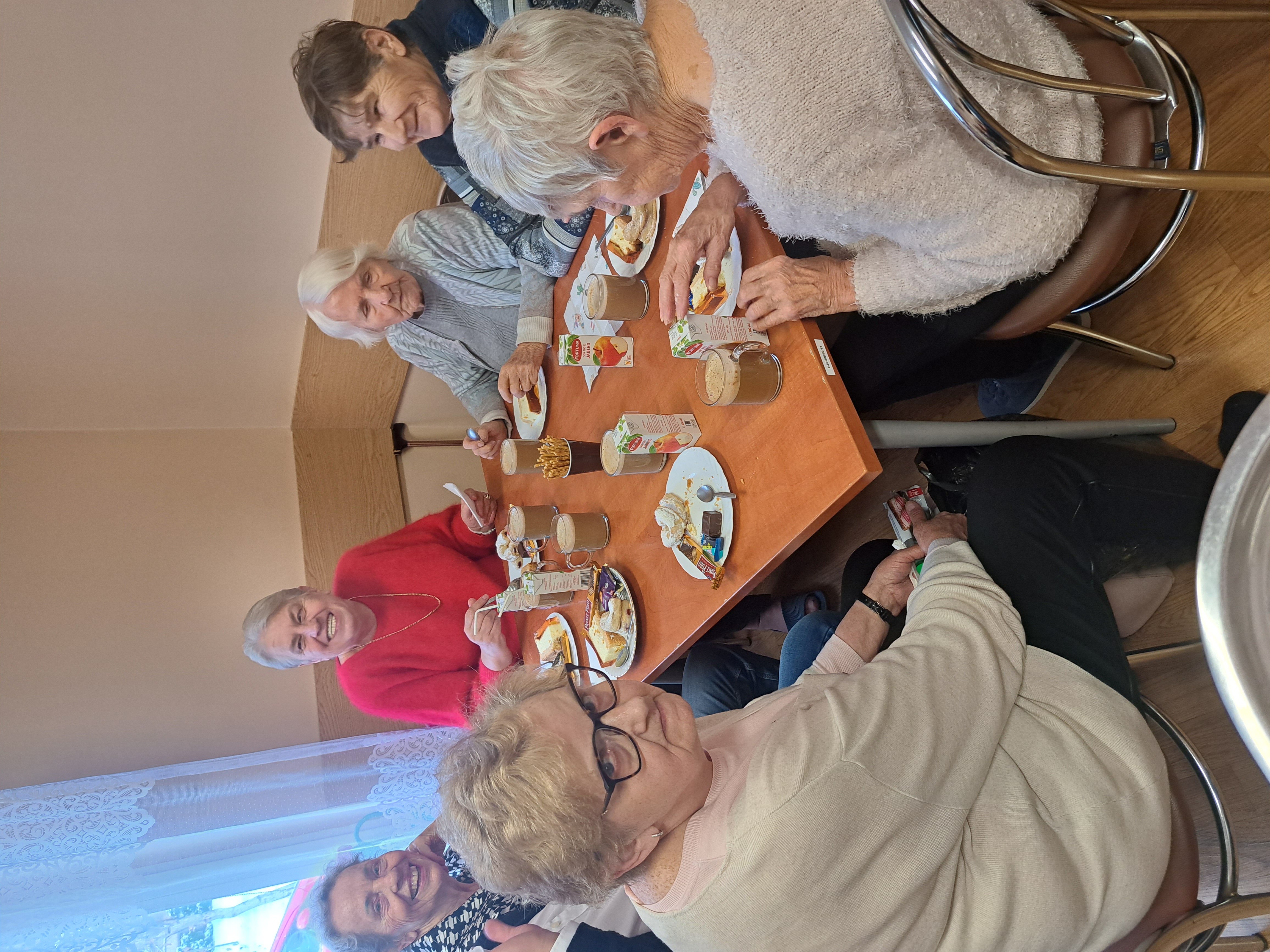 Seniorzy siedzą przy stole i jedzą słodkości