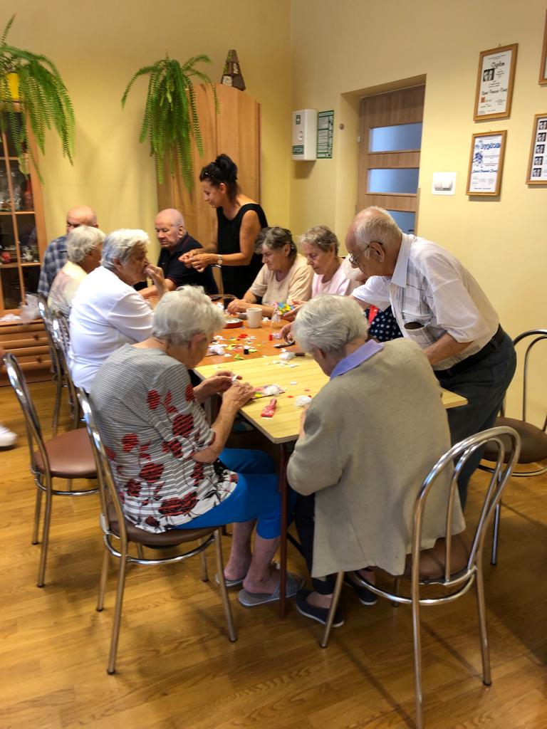 Seniorki siedzą przy stole, przed nimi stoją miski z sitkami, a w ich bukiet lawendy