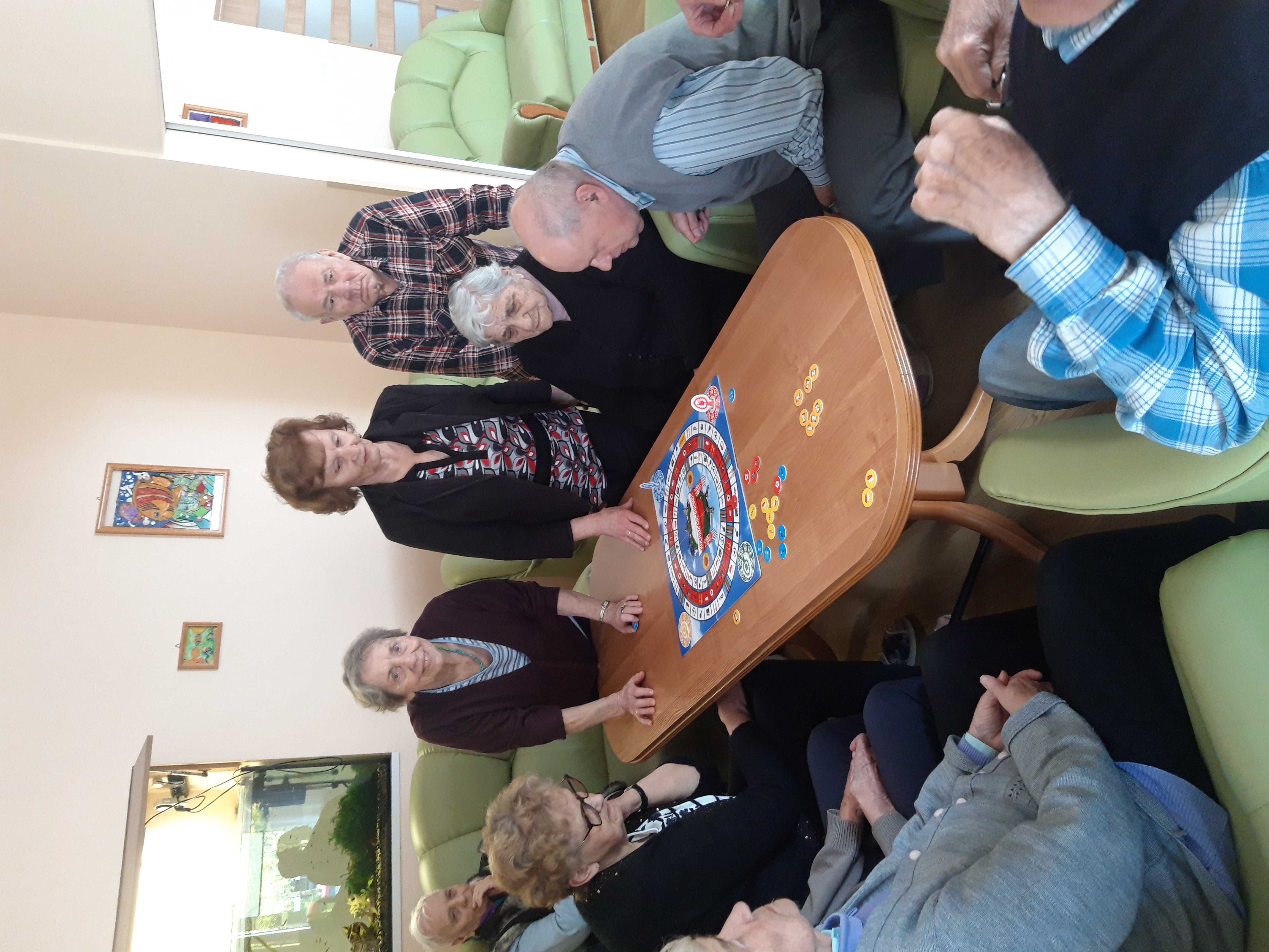Grupa Seniorów siedzi przy stole, grają w grę planszową