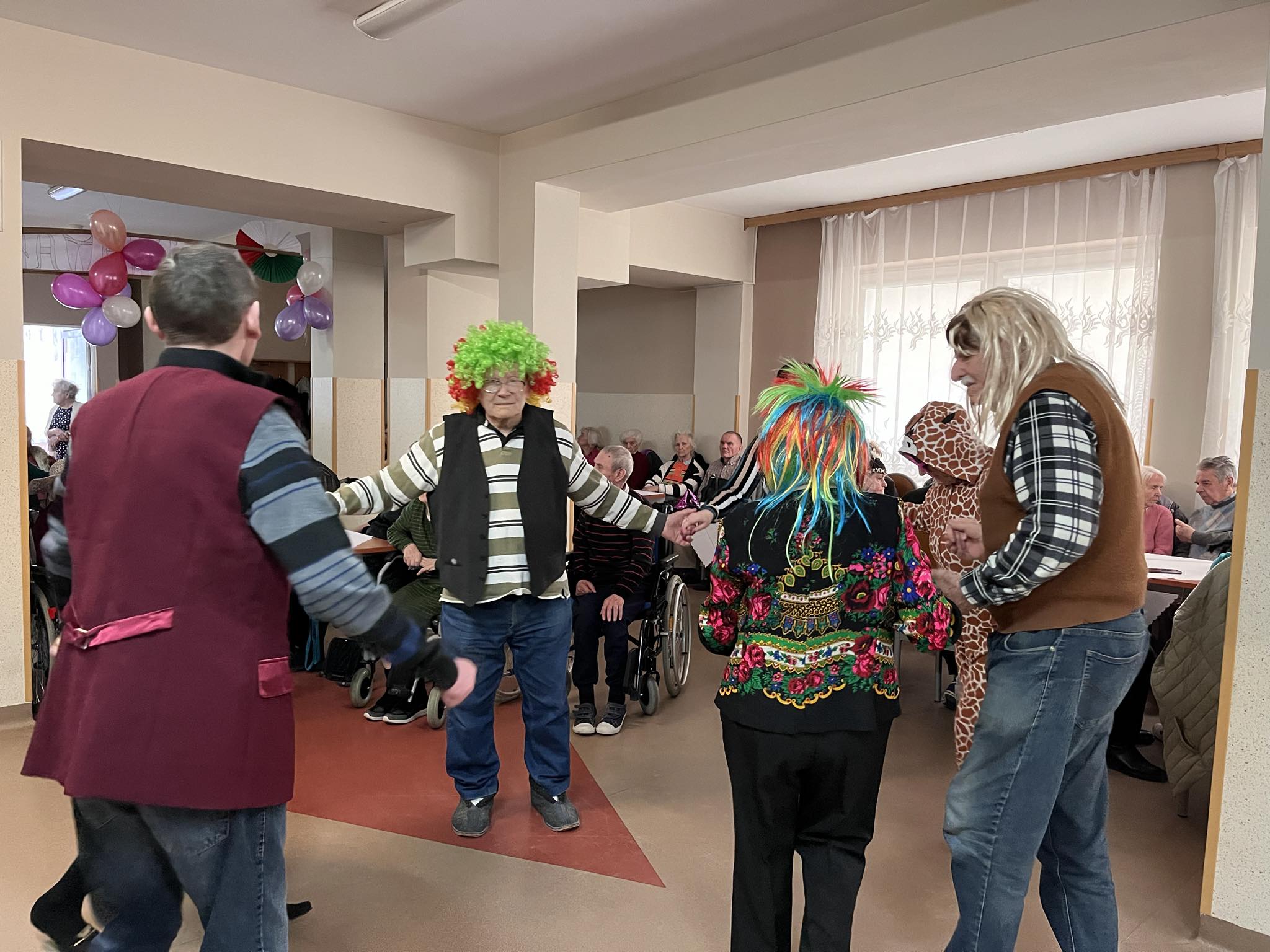 Grupa Seniorów w karnawałowych przebaniach tańczą w kółku