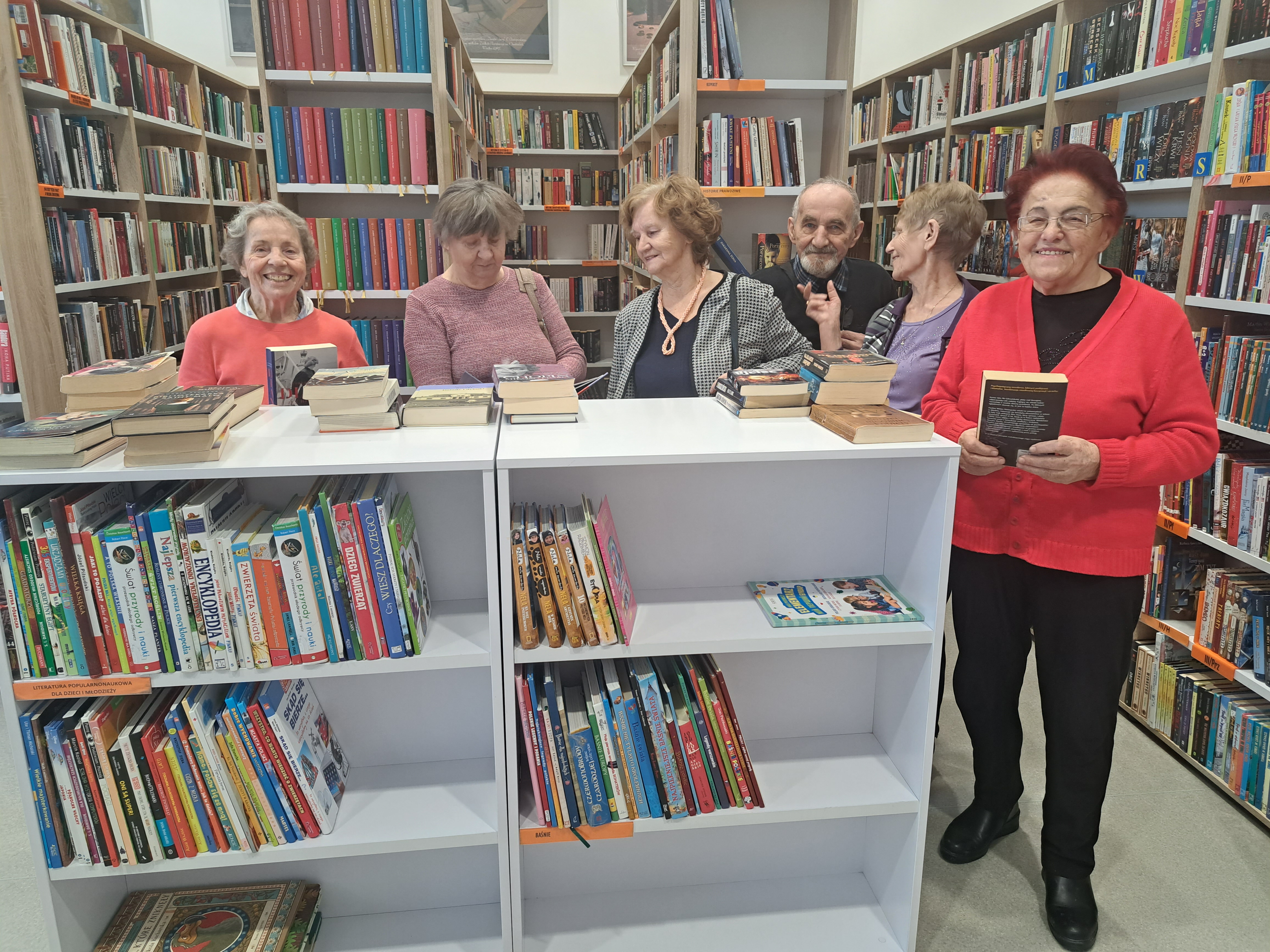 Grupa Seniorów rozgląda się za książkami w sali bibliotecznej