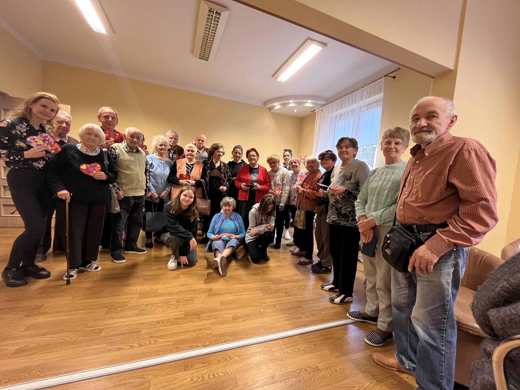 Senior pozuje ze zrobioną przez siebie kartką walentynkową, w drugiej ręce trzyma herbatę w filiżance