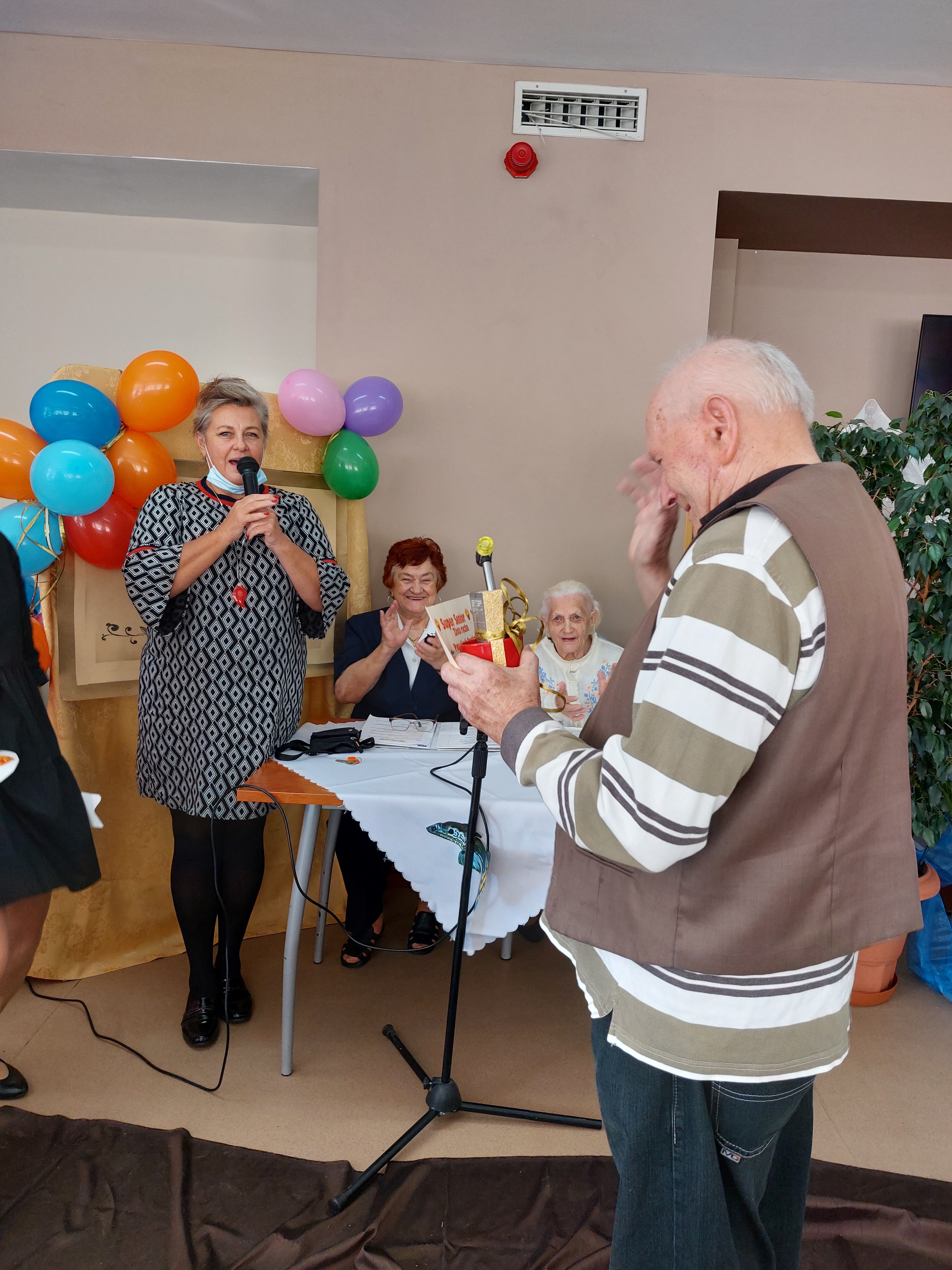 Dyrektor dps składa seniorom życzenia, stojąc na scenie