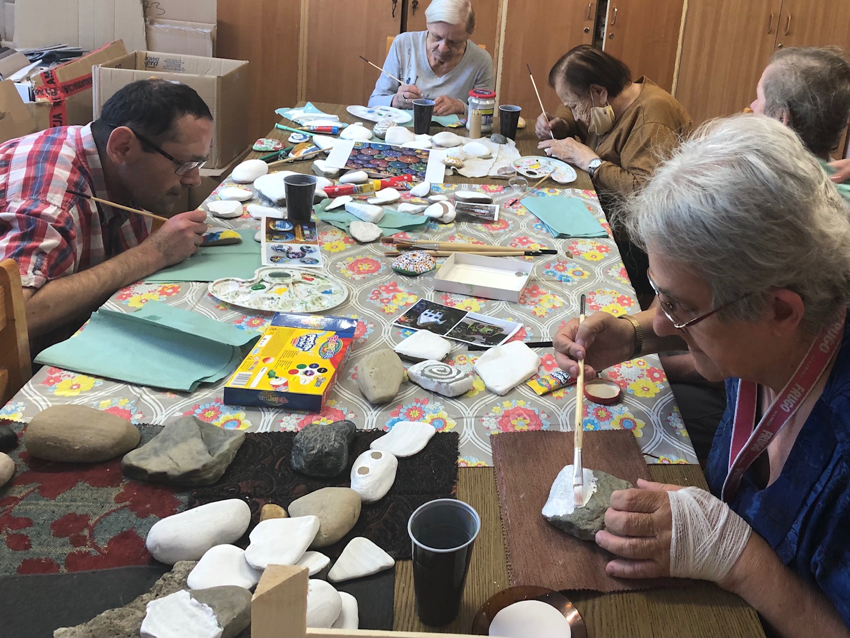 Grupa seniorów maluje kamienie przy stole