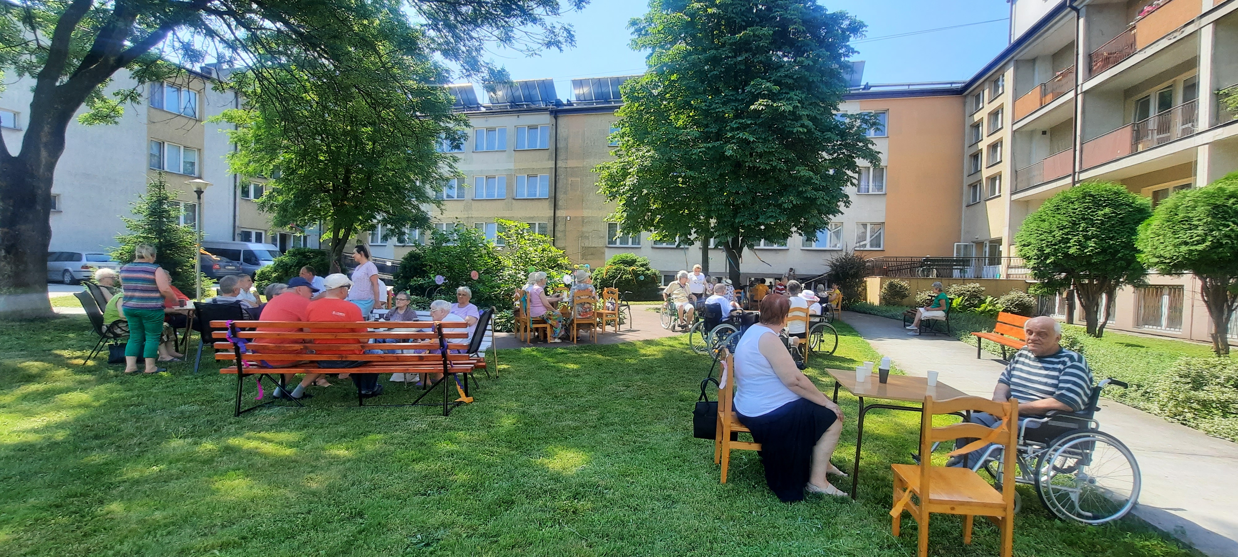 Seniorzy siedzą na wózkach w ogrodzie>