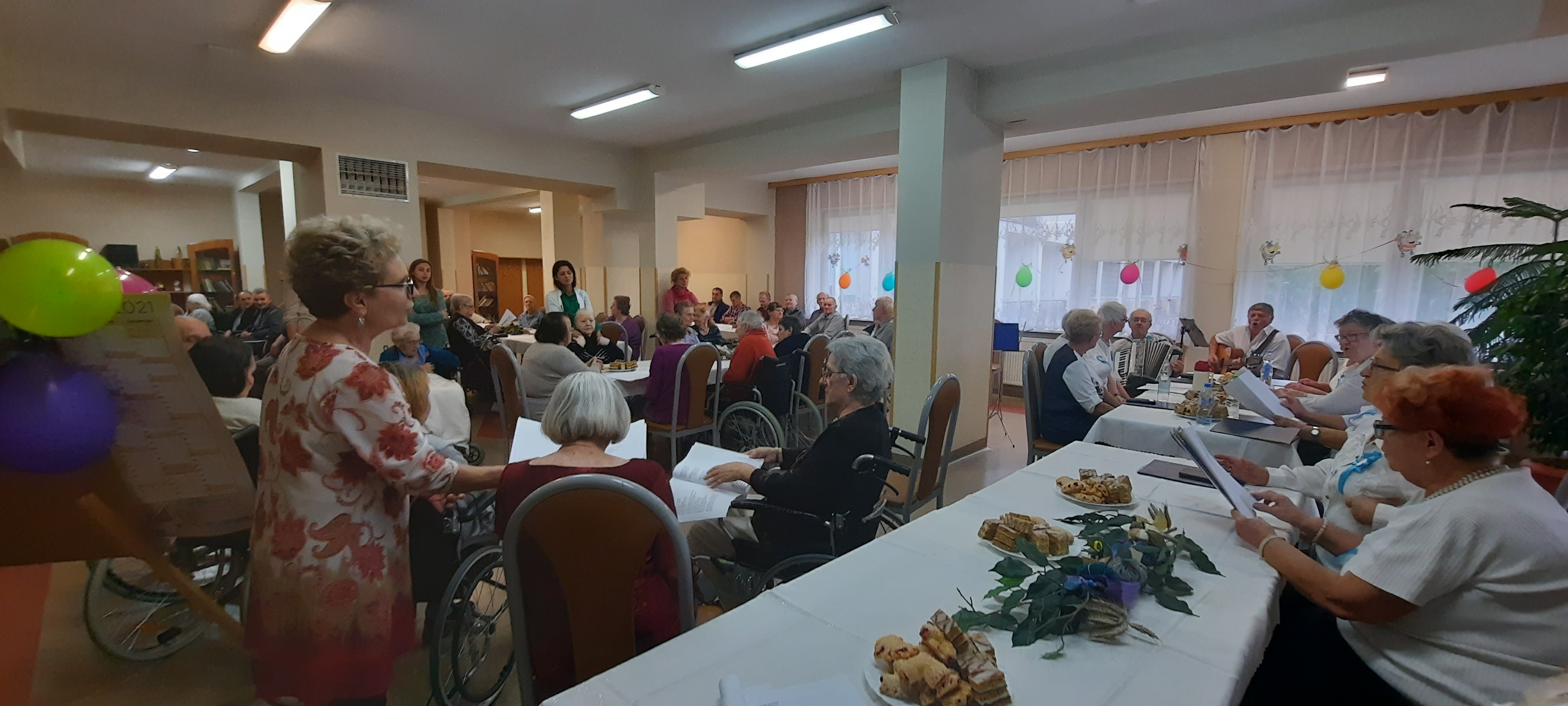 Szeroki kadr na seniorów siedzących przy stołach na świetlicy