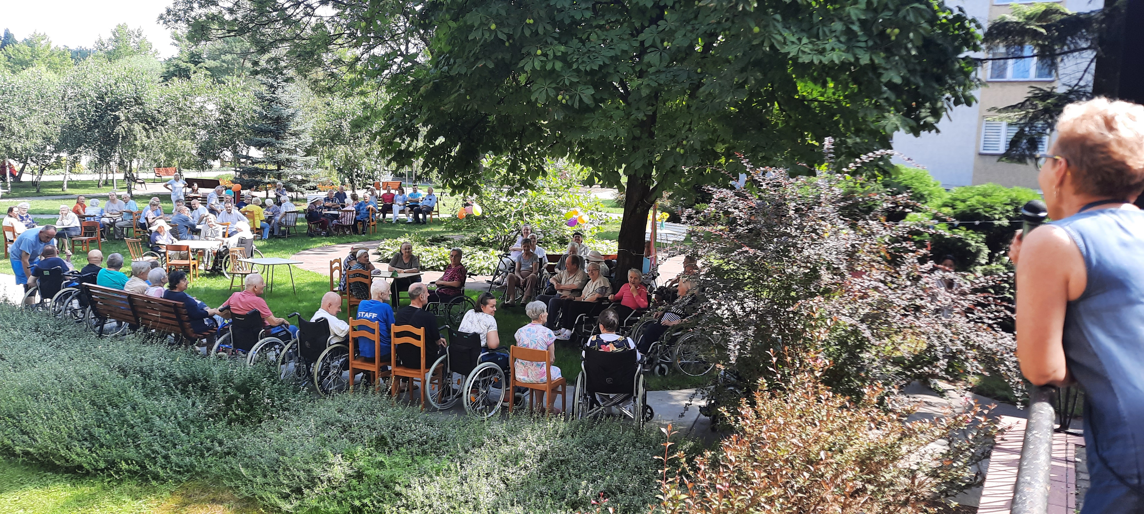 Duża grupa Seniorów siedzących w ogrodzie Domu