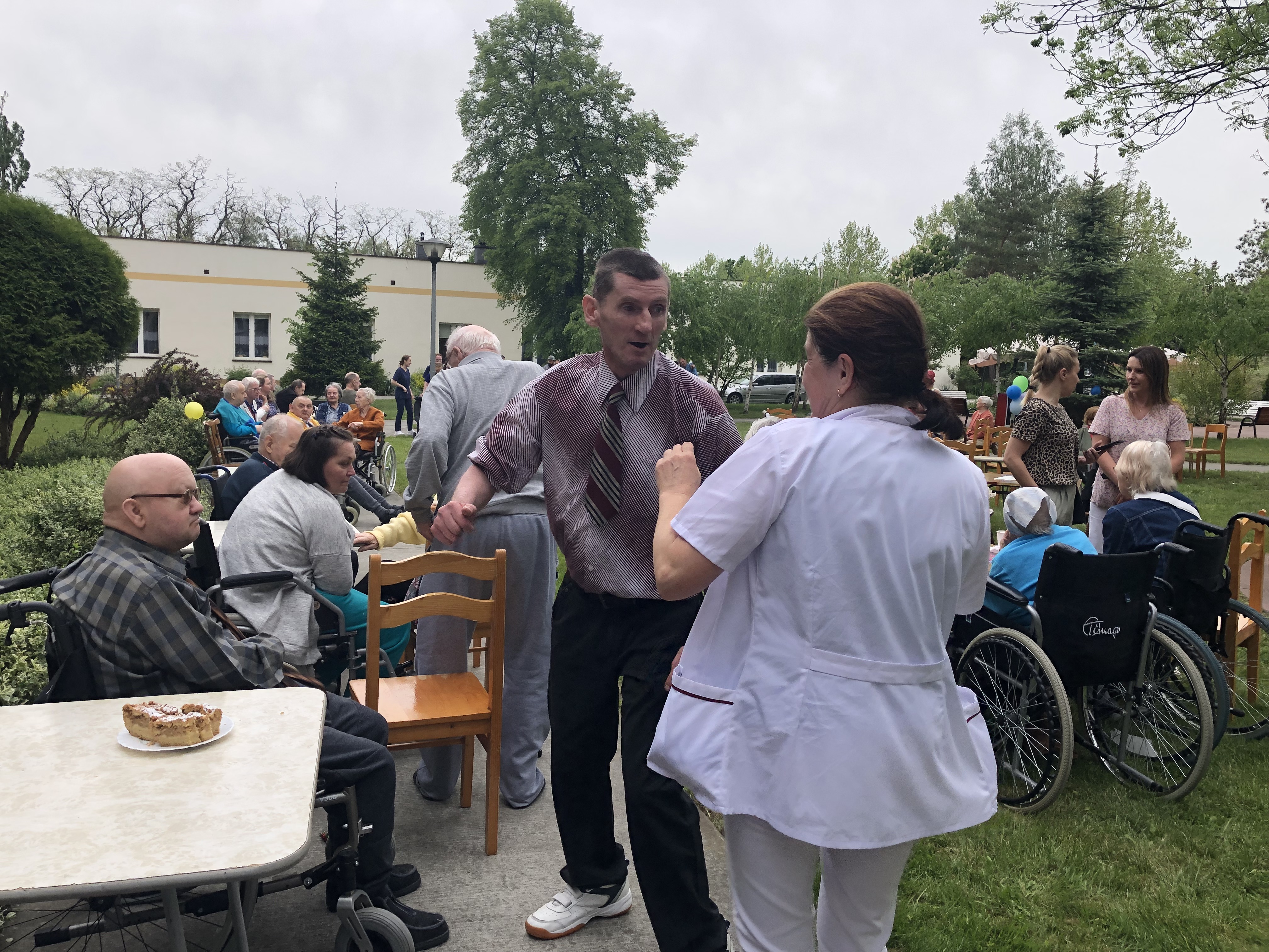 Tańczący seniorzy na pierwszym planie, w tle seniorzy siedzący przy stołach