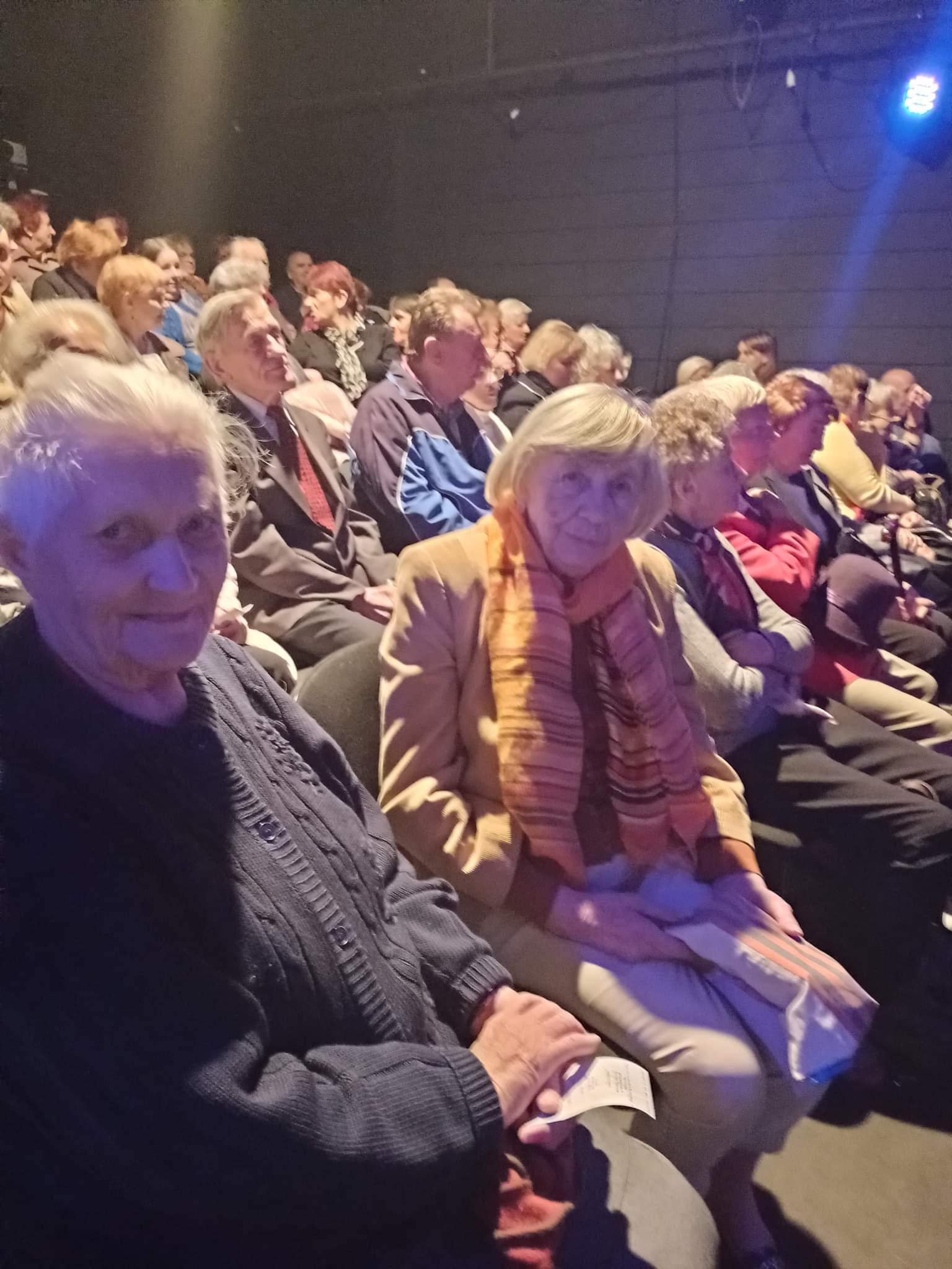 Seniorzy siedzący w pierwszym rzędzie przed sceną