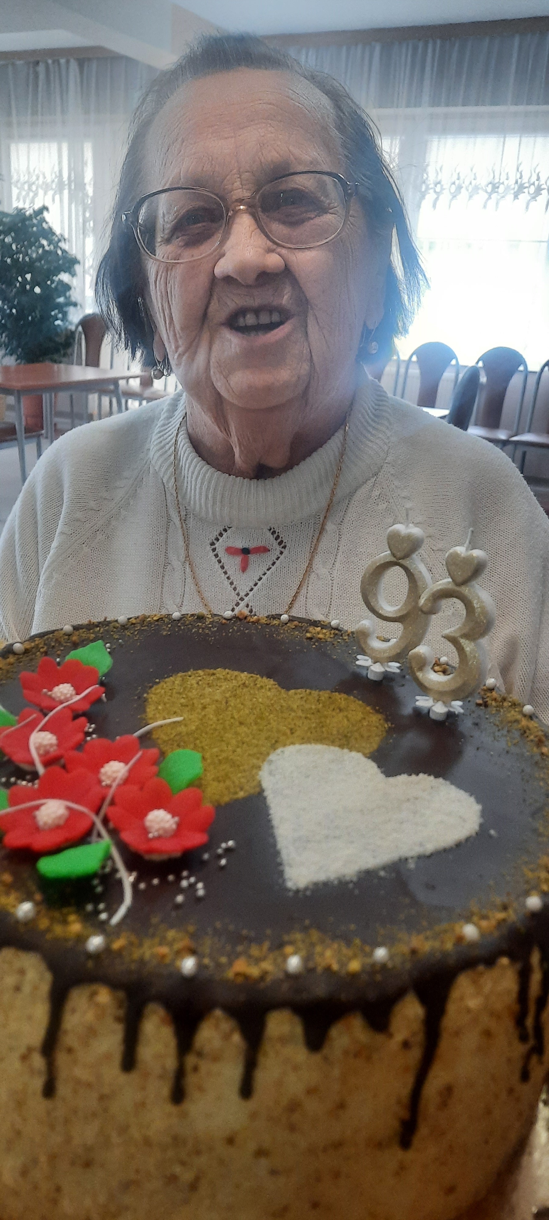 Seniorka przy stole, przed nią stoi tort z liczbą 93