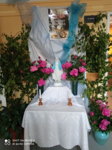 Ołtarz przyozdobiony różowymi kwiatami, na środku stoi posążek Maryi