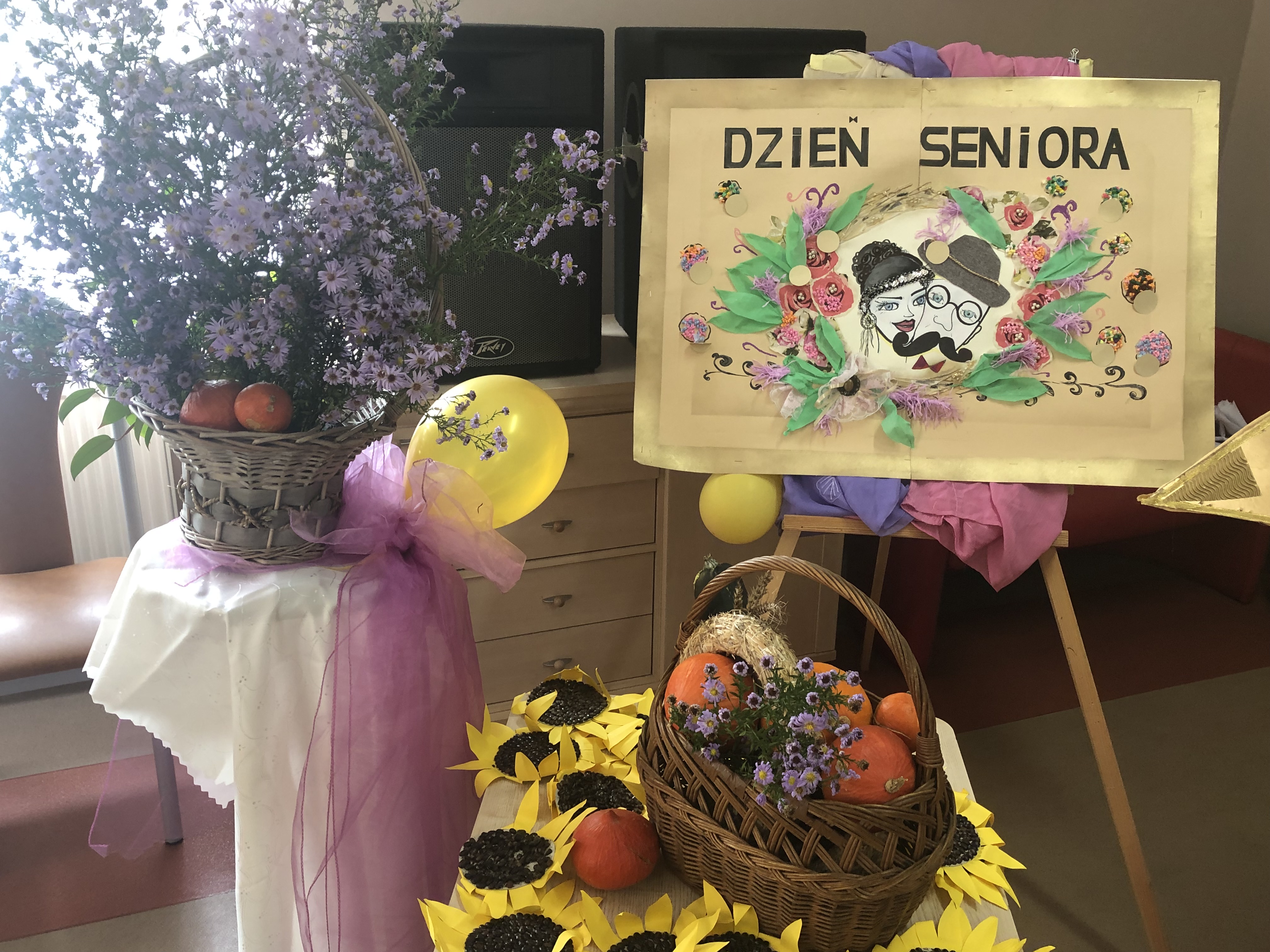 własnoręcznie zrobiona tablica z napisem Dzień Seniora, obok stoi duży bukiet kwiatów, a w nim baloniki
