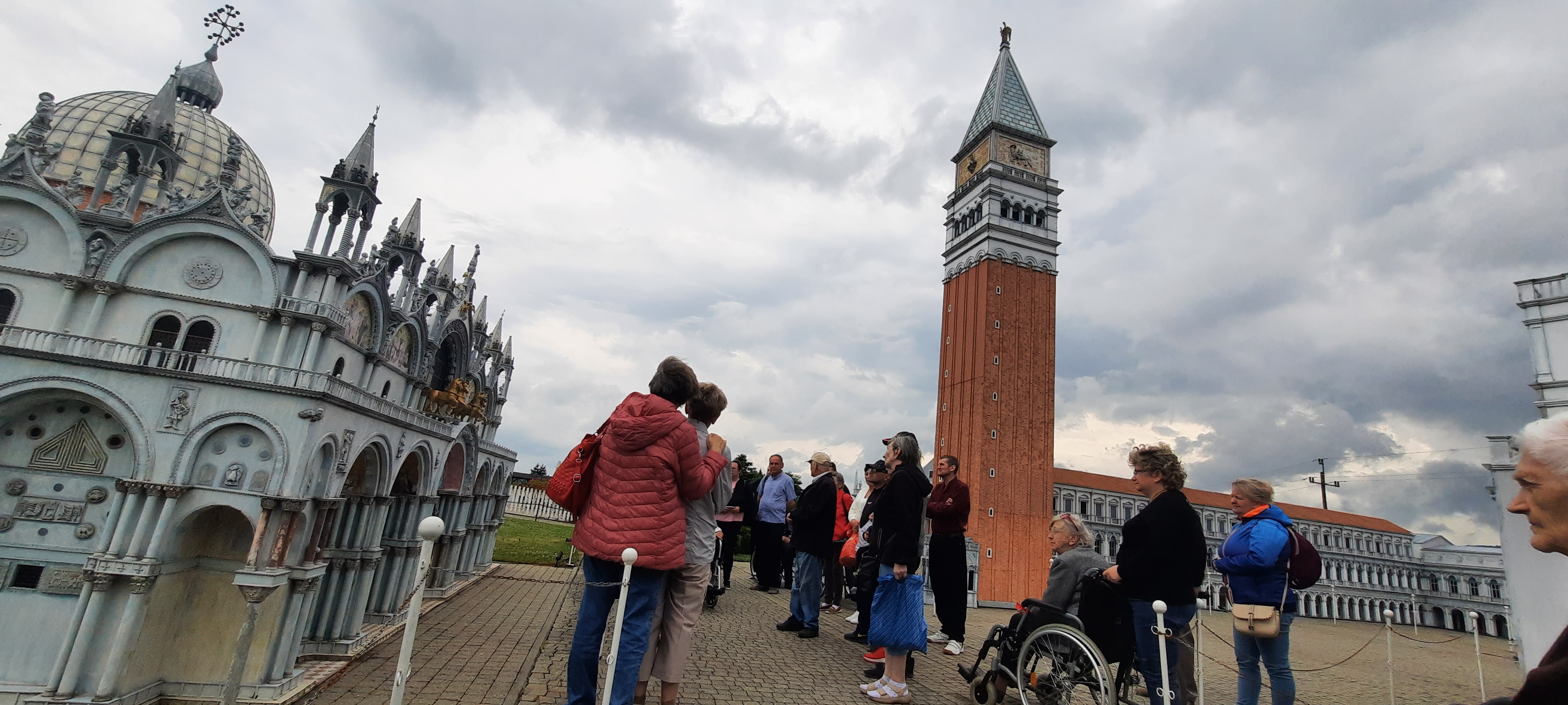 Seniorzy siedzą przy stole, ulokowanym pod dużym rozłożysztym drzewem