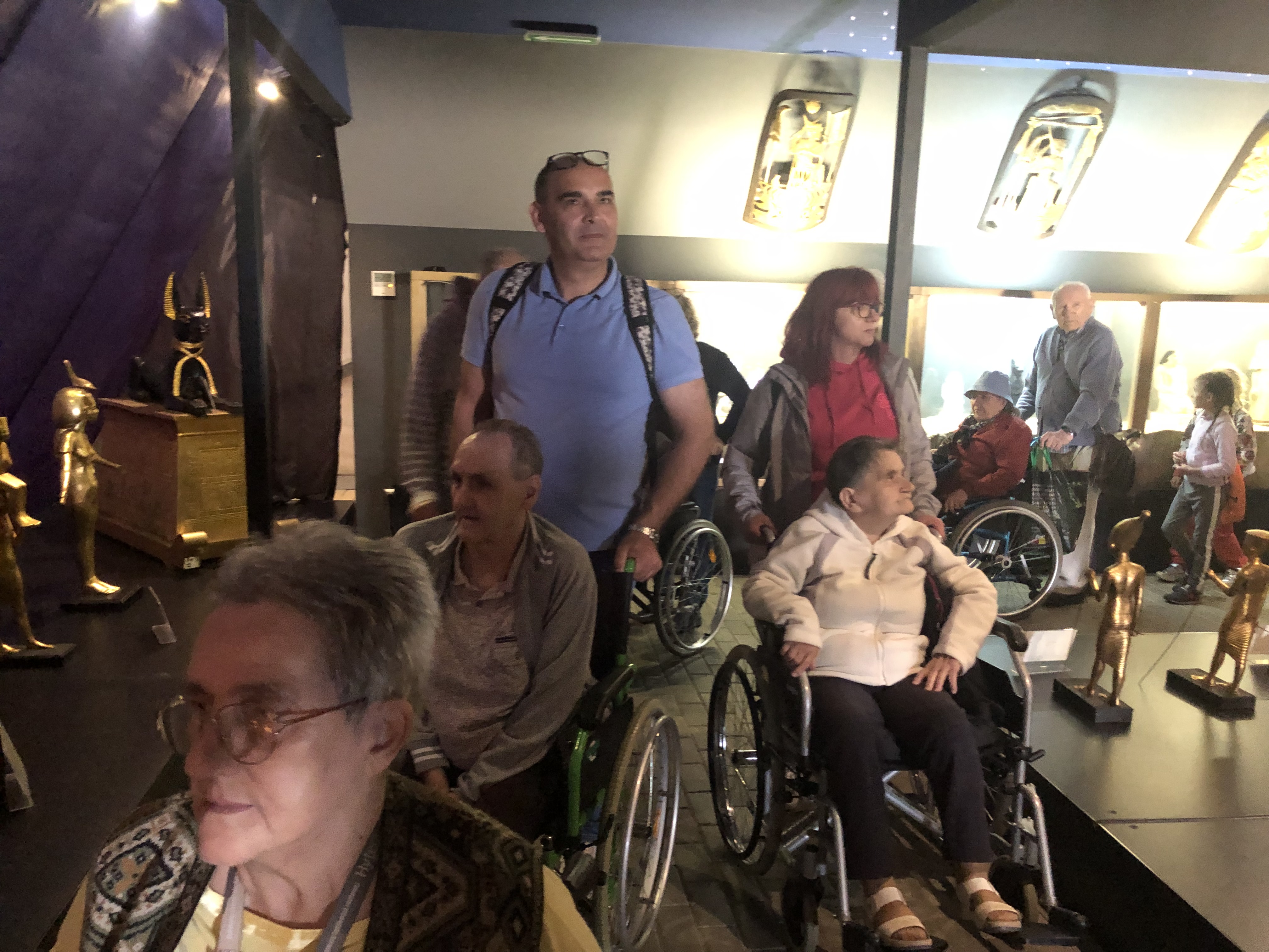 Opiekunowie pomagają Seniorom na wózkach poruszać się po wystawie miniaturowych rzeźb egipskich
