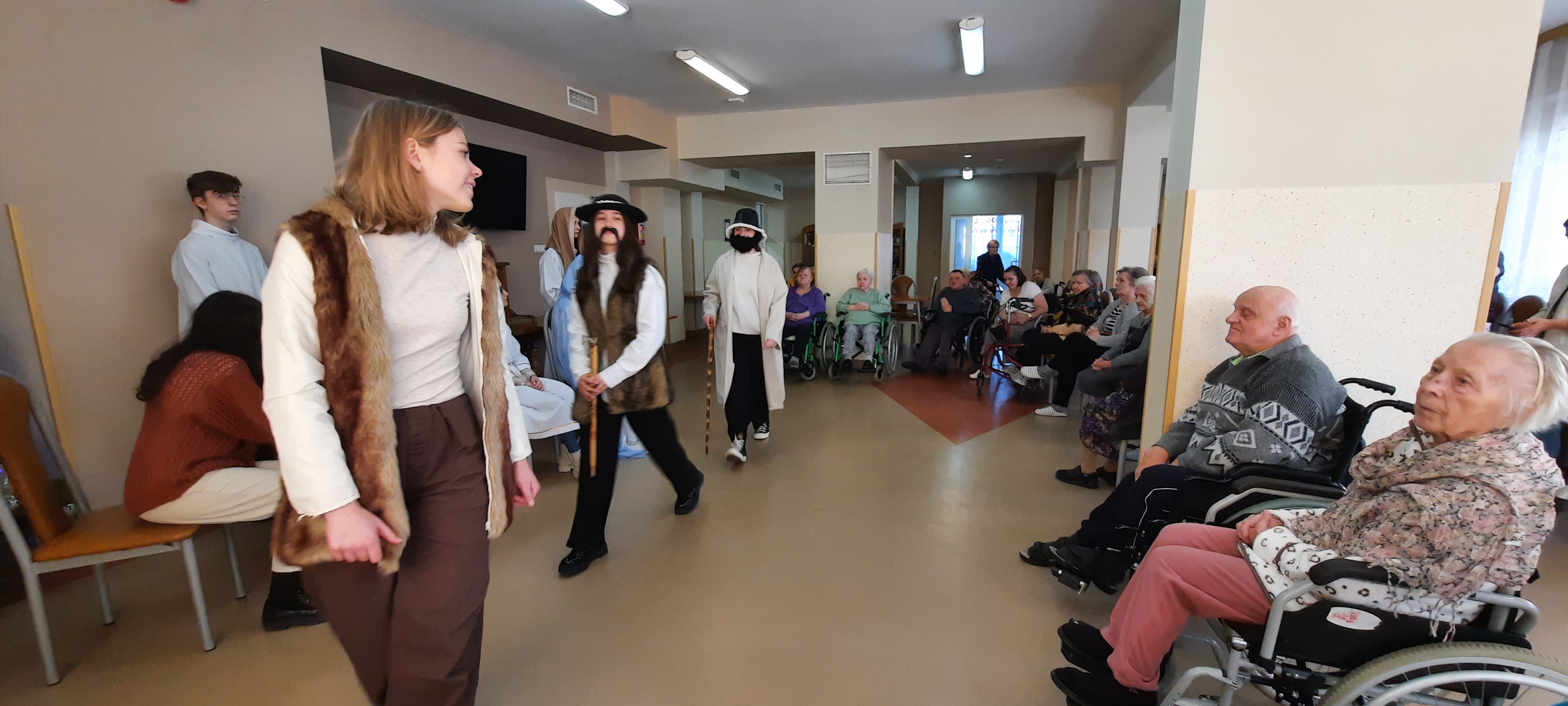 Troje nastolatków w strojach pastuszków, chodzi po scenie. Seniorzy się przyglądają