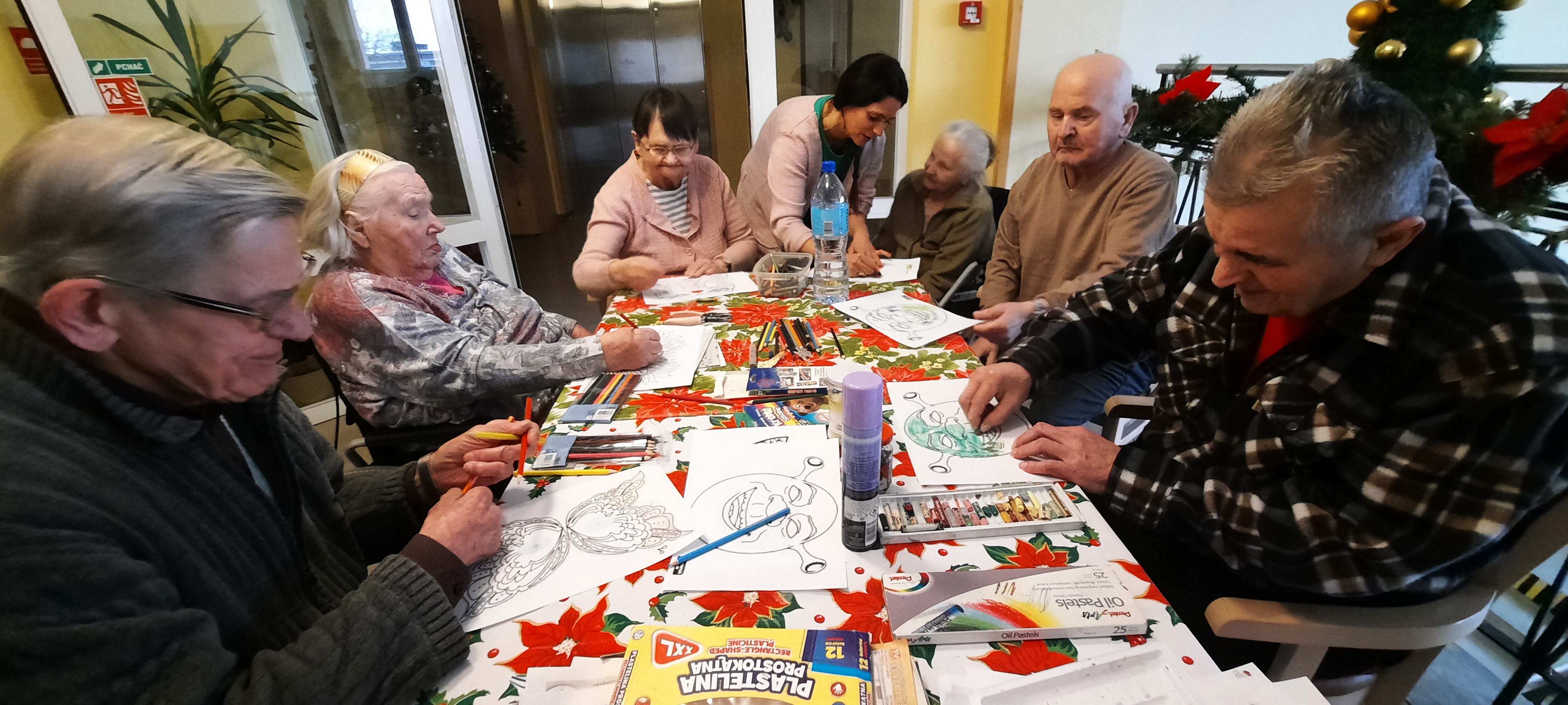 Grupa Seniorów siedzi przy stole, ozdabiają maski karnawałowe