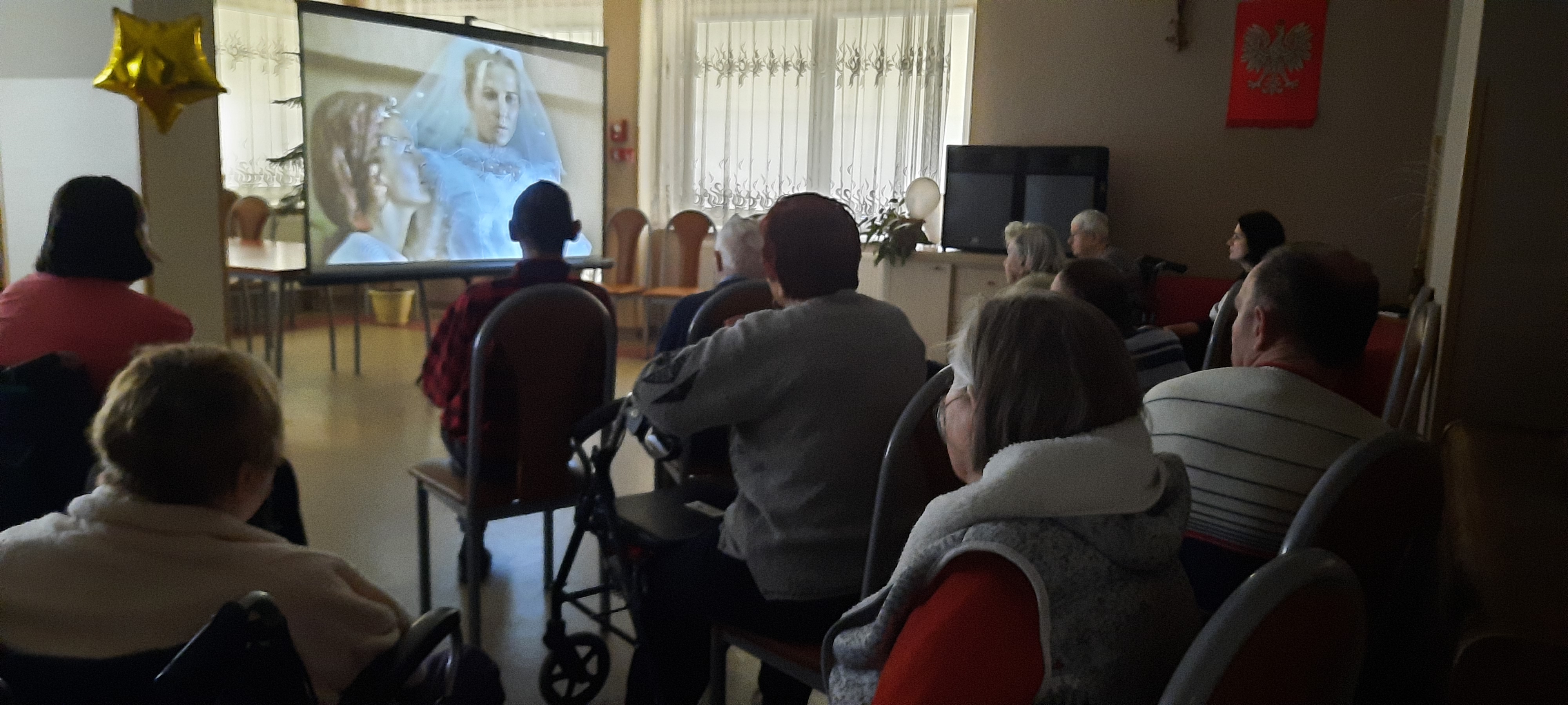 Grupa Seniorów siedzi na świetlicy, oglądają film