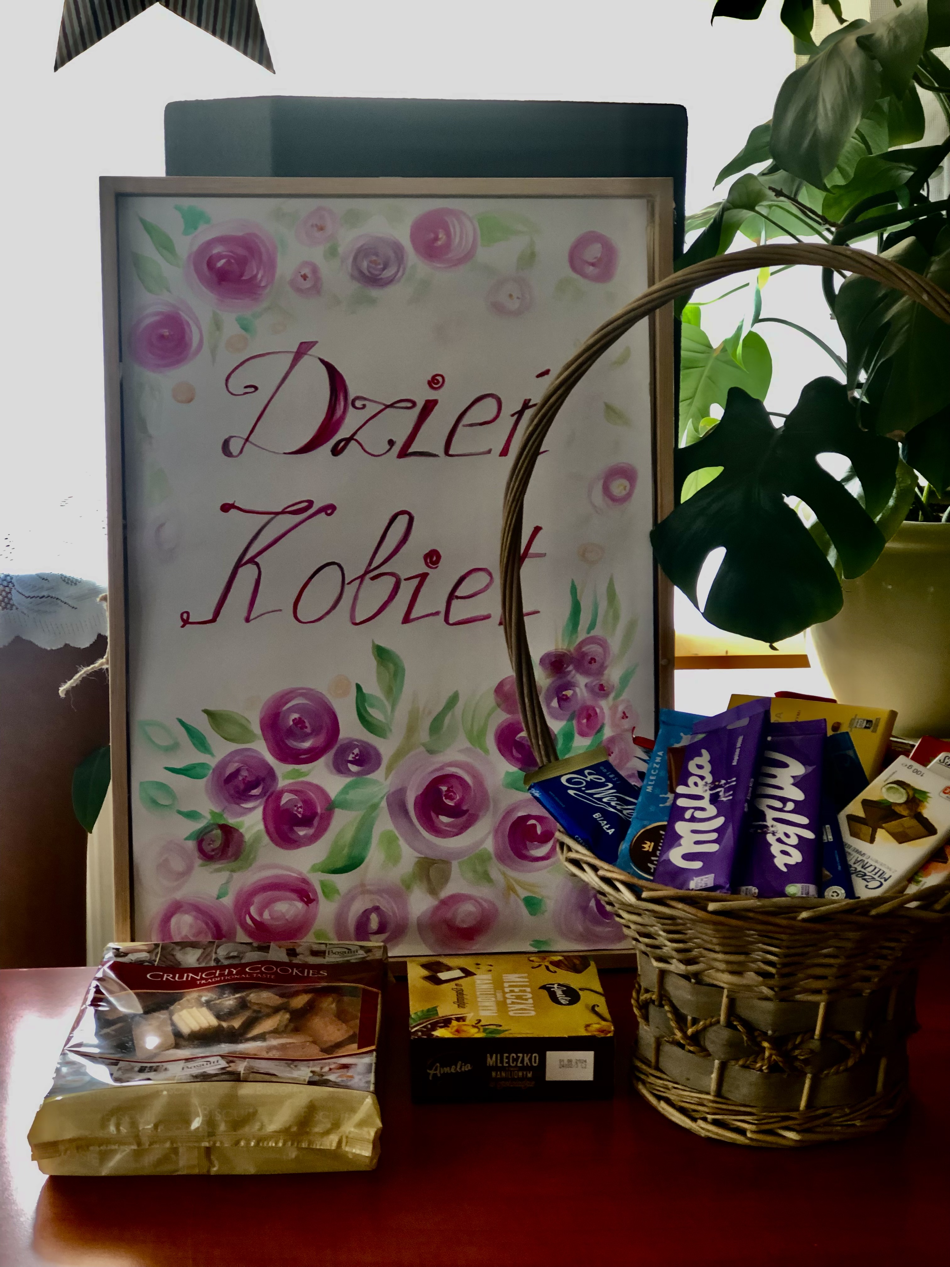 Plakat z napisem Dzień kobiet, obok stoi koszyk z czekoladami