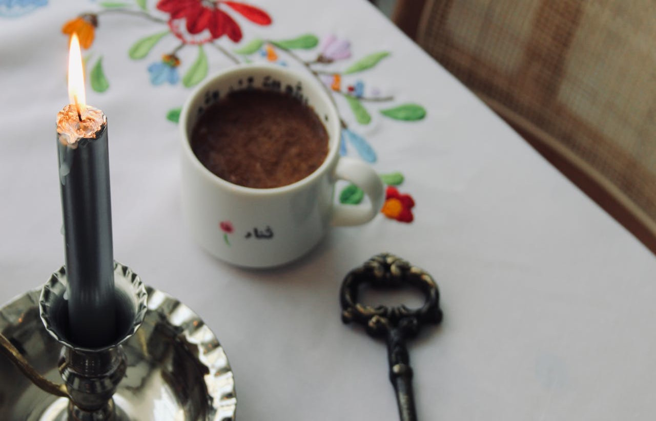 Zdjęcie czarnej świecy, klucza oraz filiżanki, znajdujących się na stole z białym obrusem