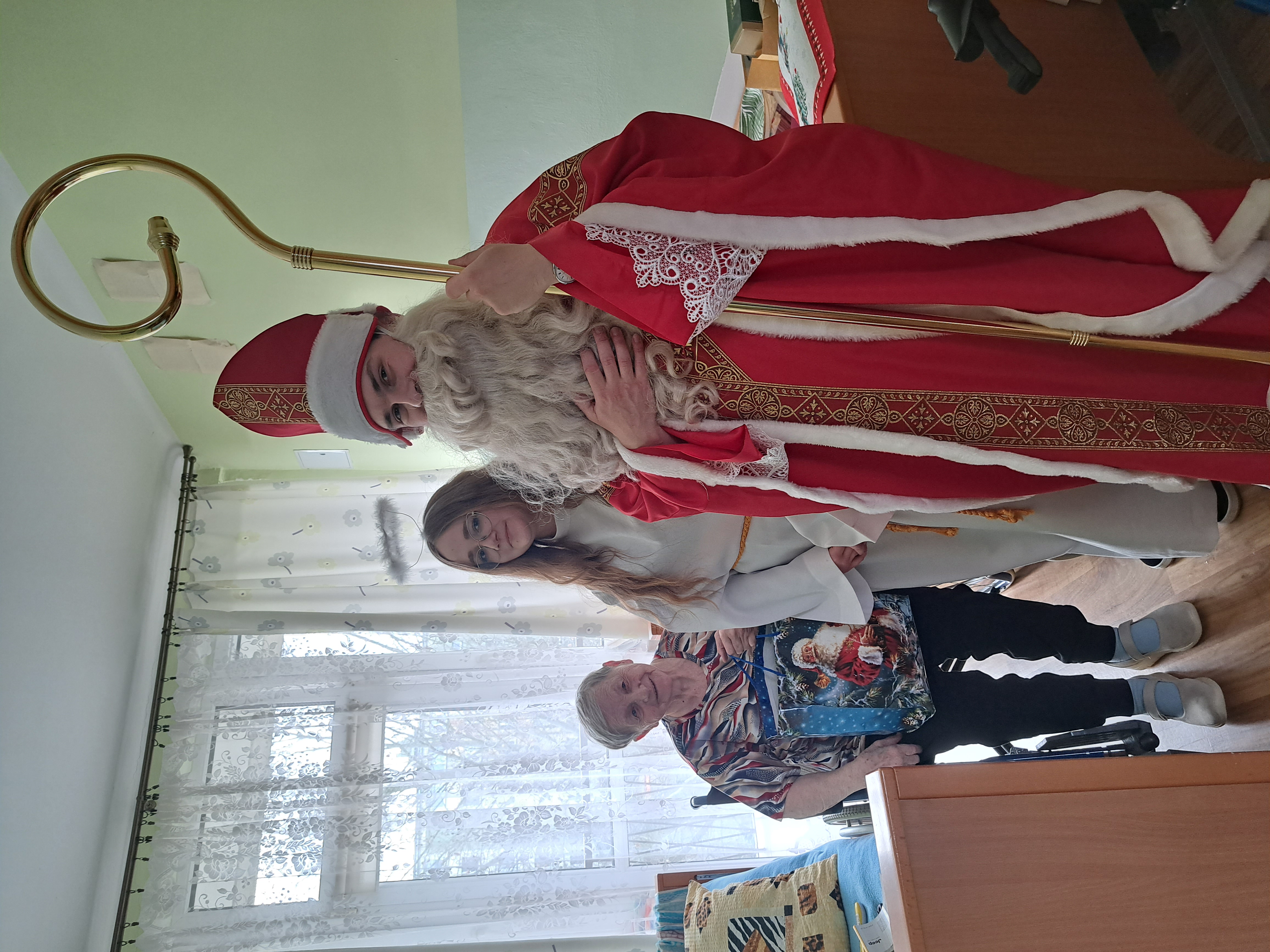 Mikołaj, dziewczyna przebrana za Aniołka oraz Seniorka trzymająca w rękach prezent od Mikołaja, pozują do zdjęcia