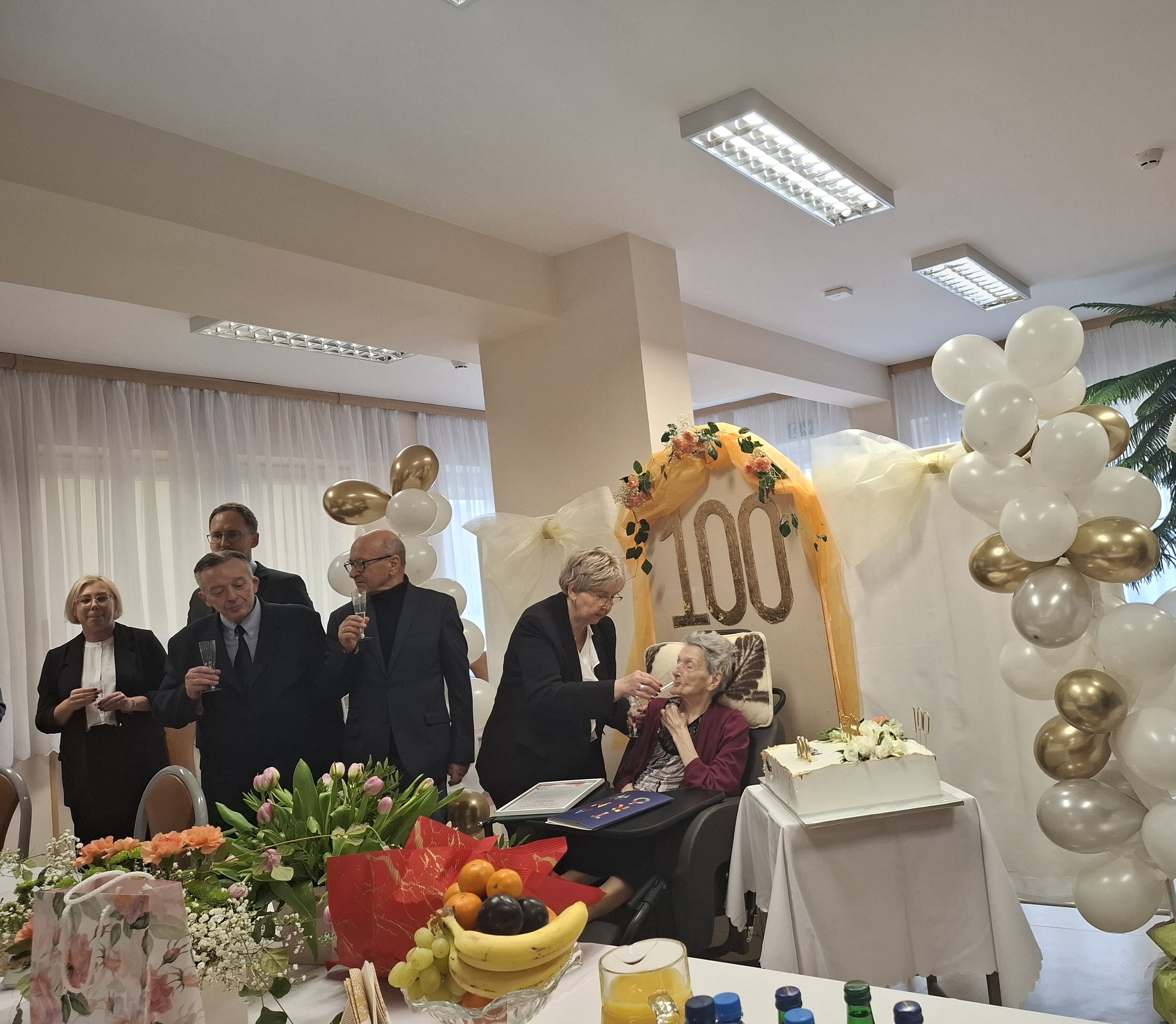 Grupowe zdjęcie Pani Zofii, pracowników Domu, Prezydenta Miasta Tarnowa. Seniorka znajduje się w centrum.