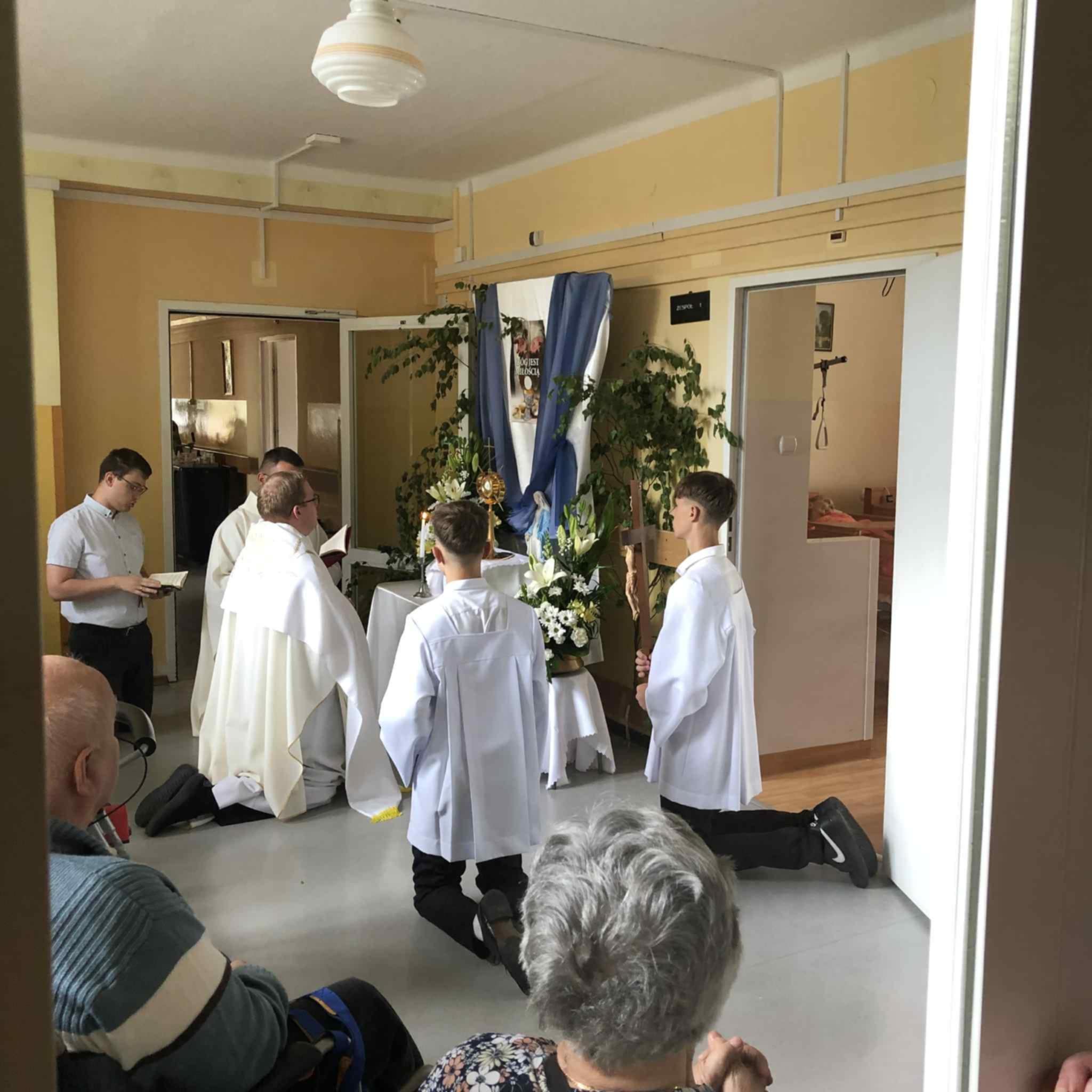 Ministranci oraz ksiądz klęczą przed ołtarzem, przygotowanym przez Dom