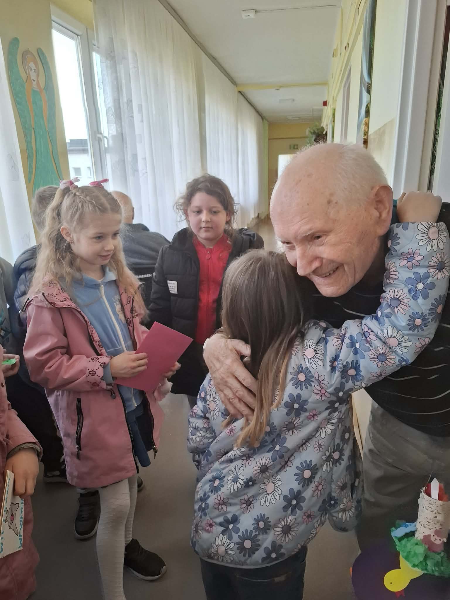 Dzieci wręczają Seniorom kartki wielkanocne, Senior obejmuje dziewczynkę w podziękowaniu za kartkęs