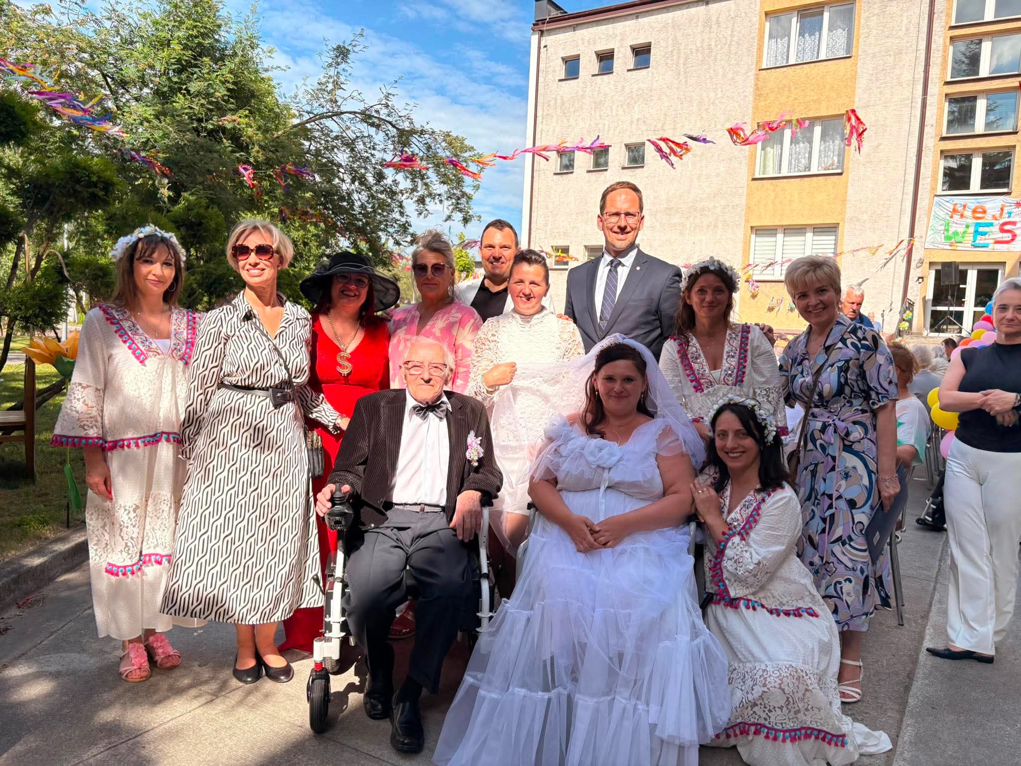 Pani Dyrektor, pracownicy Domu, Pan Prezydent oraz majówkowa Para Młoda pozują do zdjęcia w ogrodzie Domu