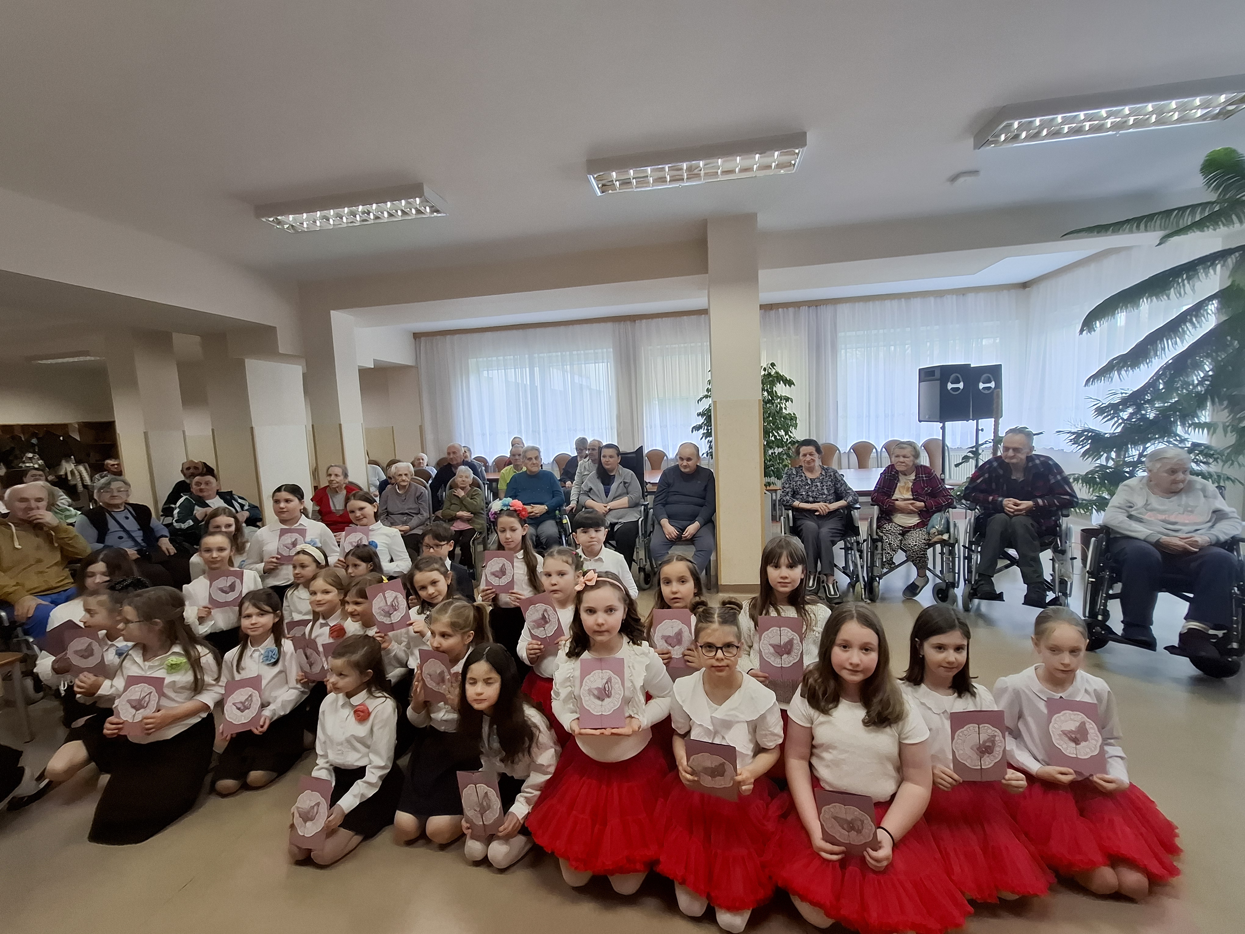 Zdjęciu grupowe oraz Seniorów, dzieci siedzą w przodu na kolanach, a Seniorzy siedzą za nimi