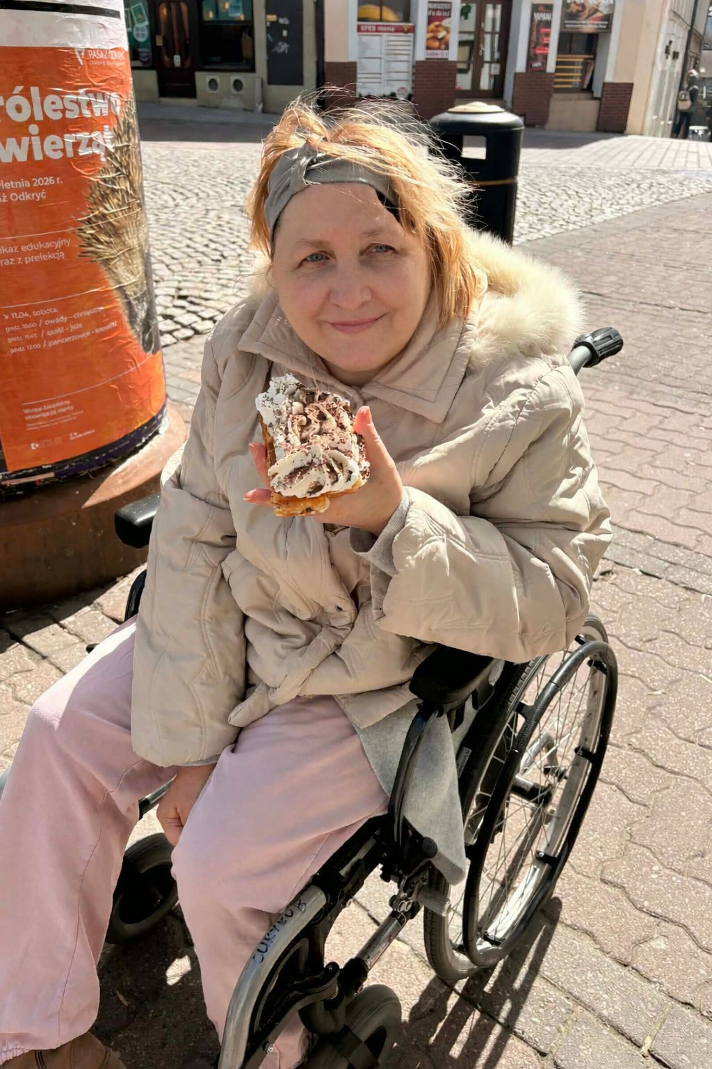 Seniorka, siedząca na wózku inwalidzkim pozuje do zdjęcia z gofrem